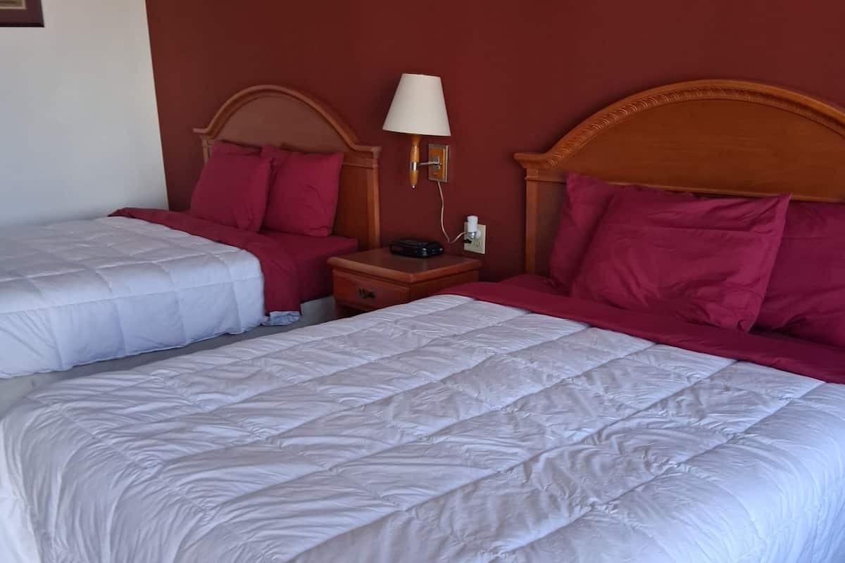 A hotel room with two beds, each with a wooden headboard, a bedside table with a lamp, and a nightstand with a phone and a remote control.