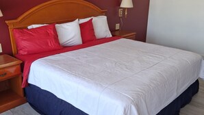 A neatly made bed with a wooden headboard, a red and white pillow arrangement, and a bedside lamp. - Coratel Inn and Suites By Jasper Anthony (Anthony)