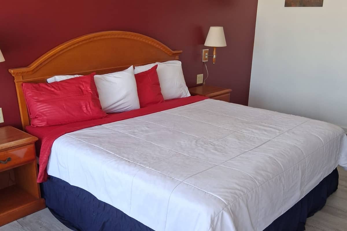 A neatly made bed with a wooden headboard, a red and white pillow arrangement, and a bedside lamp.