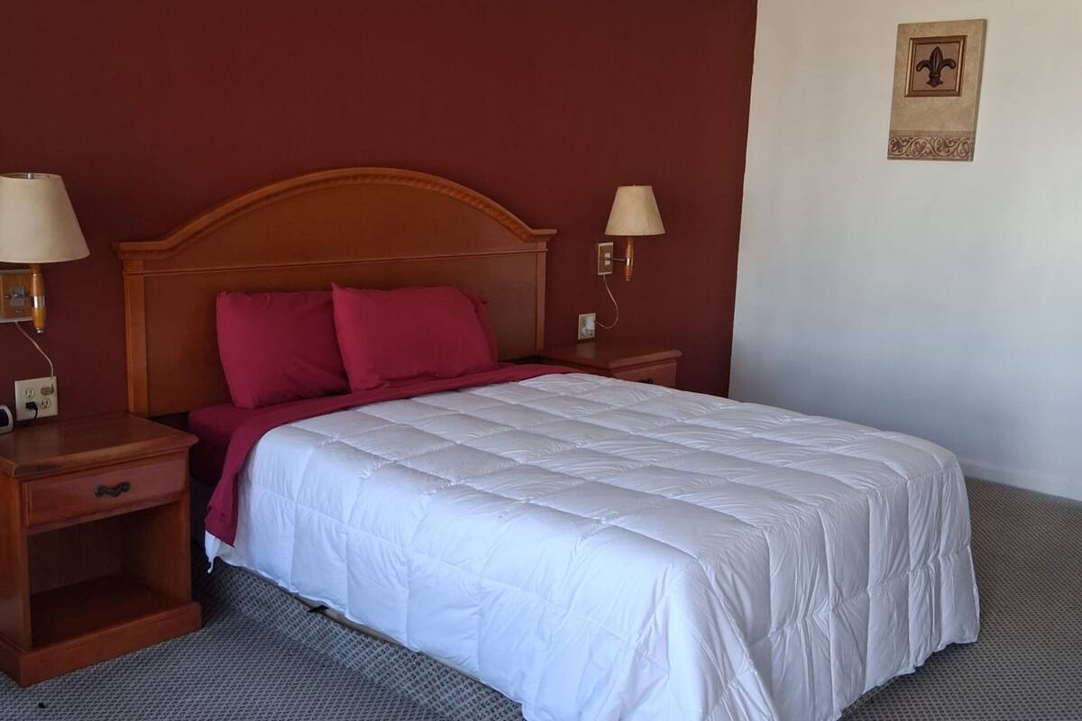 A neatly made bed with a wooden headboard, two bedside lamps, and a wall-mounted light fixture.