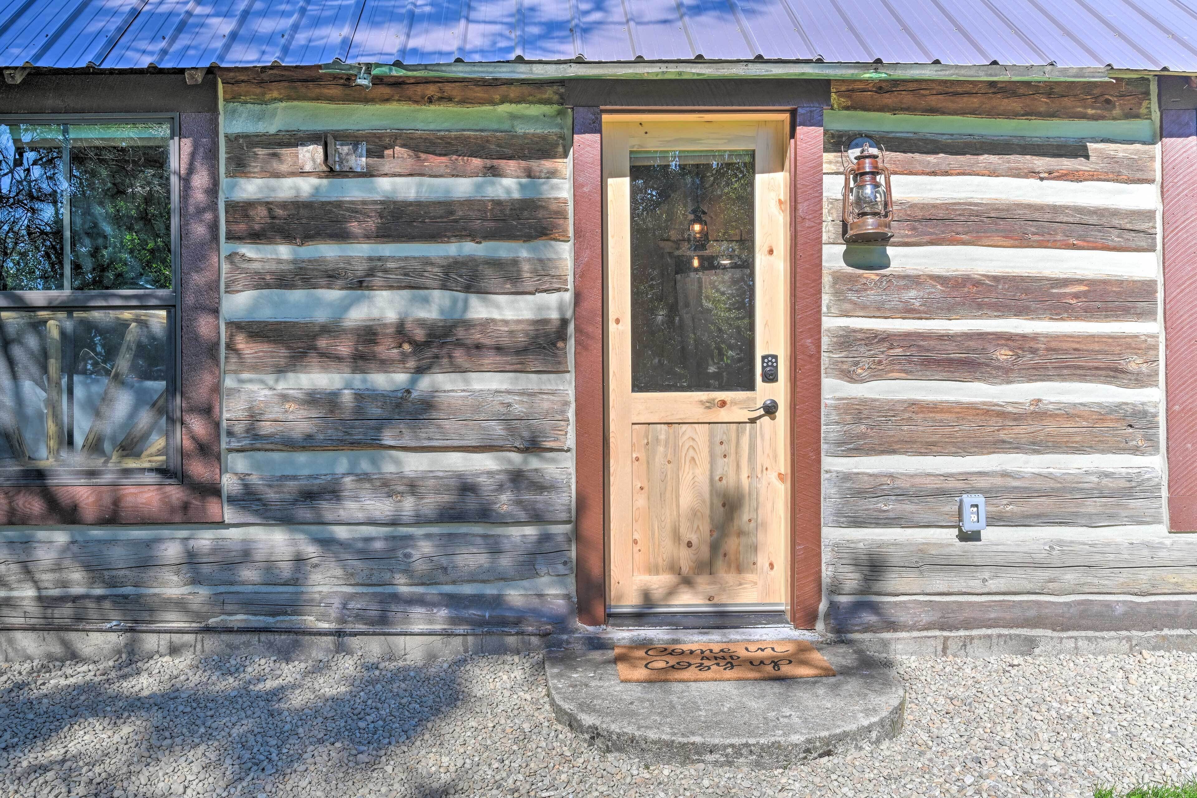 A log cabin with a wooden door, a window, and a lantern on the porch.