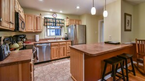 A kitchen with wooden cabinets, a stainless steel refrigerator, a sink, and a bar area with stools. - Creekside Cottage Star 5 Vacations (Black Mountain)