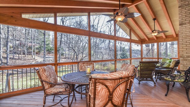 A covered outdoor deck with a round table and chairs, large windows, and ceiling fans. - Creekside Cottage Star 5 Vacations (Black Mountain)