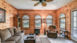 A cozy log cabin interior with a sofa, armchair, fireplace, and large windows. - Creekside Cottage Star 5 Vacations (Black Mountain)