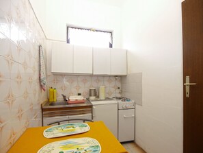 Una cocina pequeña con armarios blancos, una estufa a gas, un lavamanos y una ventana sobre el lavamanos.