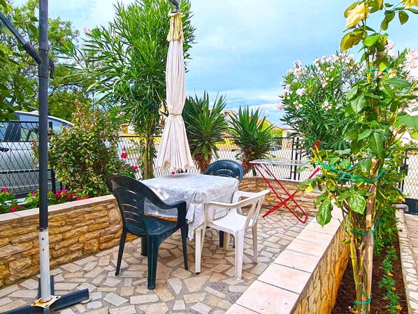 Un patio al aire libre con una mesa y sillas, rodeado de plantas y un muro de piedra.