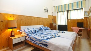 Ein Schlafzimmer mit einem hölzernen Kopfteil, einem Bett mit blauer und weißer Bettwäsche, einem Nachttisch mit Lampe, einem Fernseher auf einem Schrank und einem Fenster mit Vorhängen.