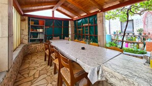 Eine überdachte Terrasse mit Steinboden, Holzmöbeln und einem Essplatz.