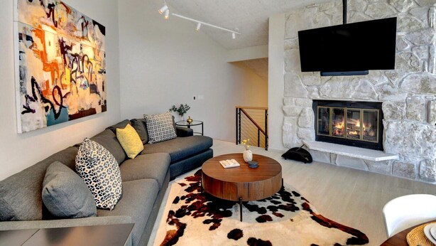 A modern living room with a stone fireplace, a large abstract painting, and a sofa with patterned cushions.