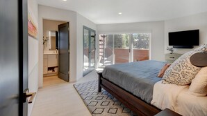 A bedroom with a large bed, a TV, and a sliding glass door leading to a balcony.