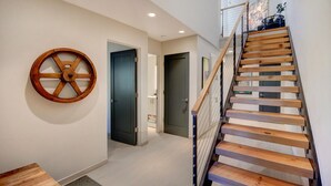 A modern interior with a wooden staircase, a round wooden wheel on the wall, and a door leading to a bathroom.