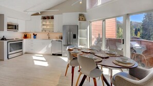 A modern kitchen with white cabinetry, a dining area with a table set for four, and large windows offering a view of the outdoors.