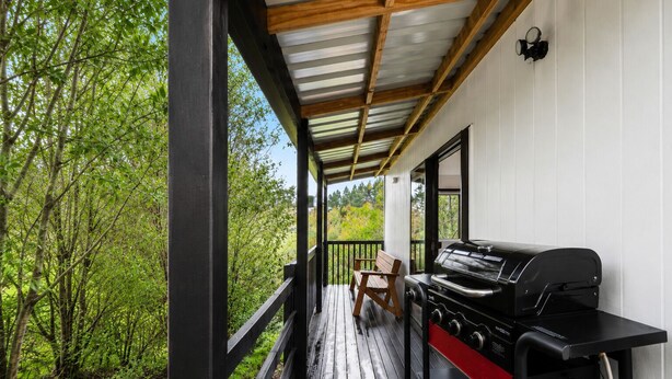 Eine überdachte Terrasse im Freien mit Grill, Bank und Blick auf einen Wald.