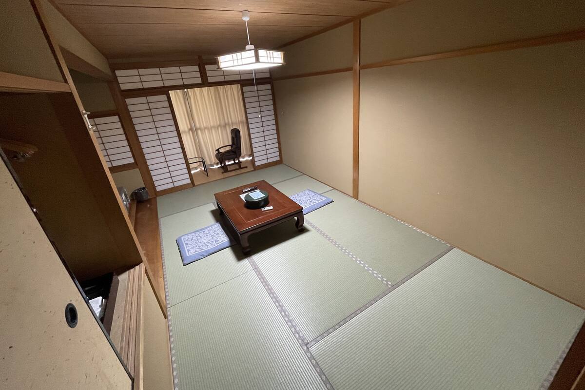 Une pièce de style japonais traditionnel, avec un sol recouvert de tatamis, une basse table en bois, un luminaire au plafond et des portes coulissantes.