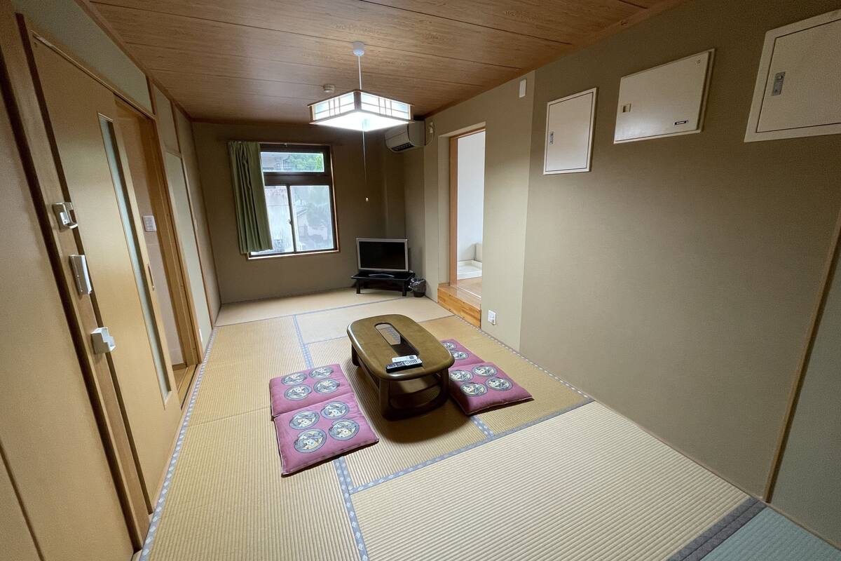 Une pièce de style japonais traditionnel, avec un sol recouvert de tatamis, un futon servant de lit, une télévision et un ventilateur de plafond.