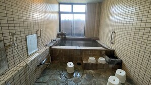 A traditional Japanese onsen with a stone floor, a large soaking tub, and a window providing a view of the outside. - Hotel Isodokei (Shirahama)