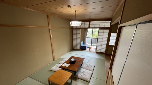 A traditional Japanese room with tatami flooring, a low wooden table, and a small stool. - Hotel Isodokei (Shirahama)