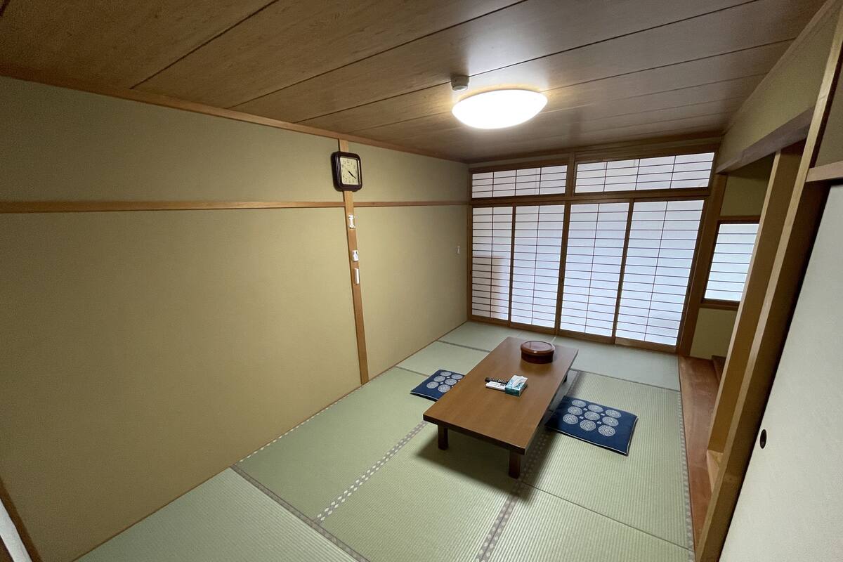 Une pièce de style japonais traditionnel, avec un sol recouvert de tatamis, une petite table en bois, une horloge au mur et des paravents en papier.