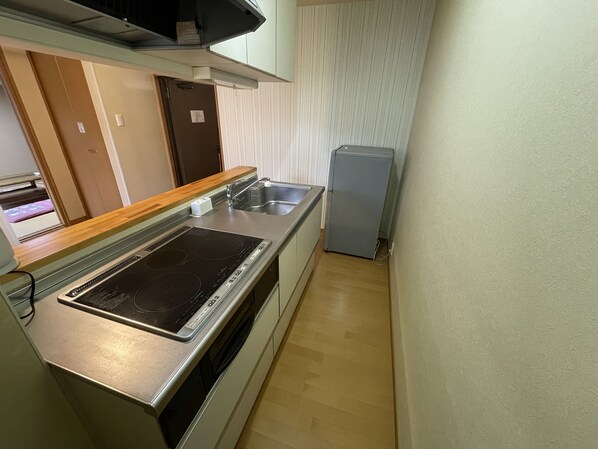 A compact kitchen with a built-in stove, a sink, and a small refrigerator. - Hotel Isodokei (Shirahama)