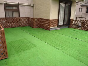 A green artificial turf patio area with wooden lattice fencing, a door, and a window. - Hotel Isodokei (Shirahama)