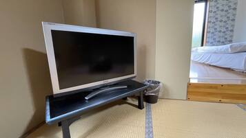 A television on a stand in a room with a bed and a window.