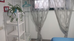 A room with a white shelving unit, a potted plant, and sheer curtains with a leaf pattern. - Laura's house 50 meters from the sea (giardini naxos)