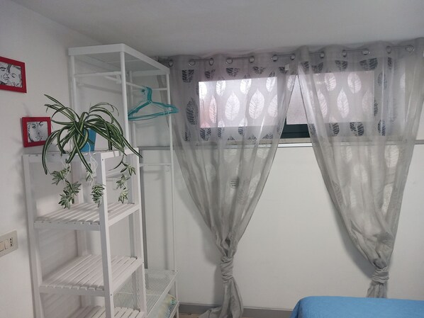 Una habitación con un estante blanco, una planta en maceta y cortinas traslúcidas con diseño de hojas.
