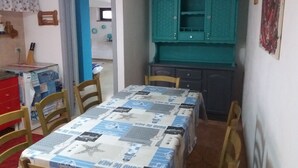 A compact dining area with a table covered in a patchwork tablecloth, wooden chairs, and a teal cabinet with open doors. - Laura's house 50 meters from the sea (giardini naxos)
