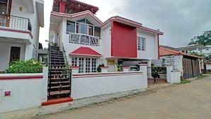 Une maison à deux étages, avec une façade rouge et blanche, une entrée fermée par un portail et un balcon bien visible.