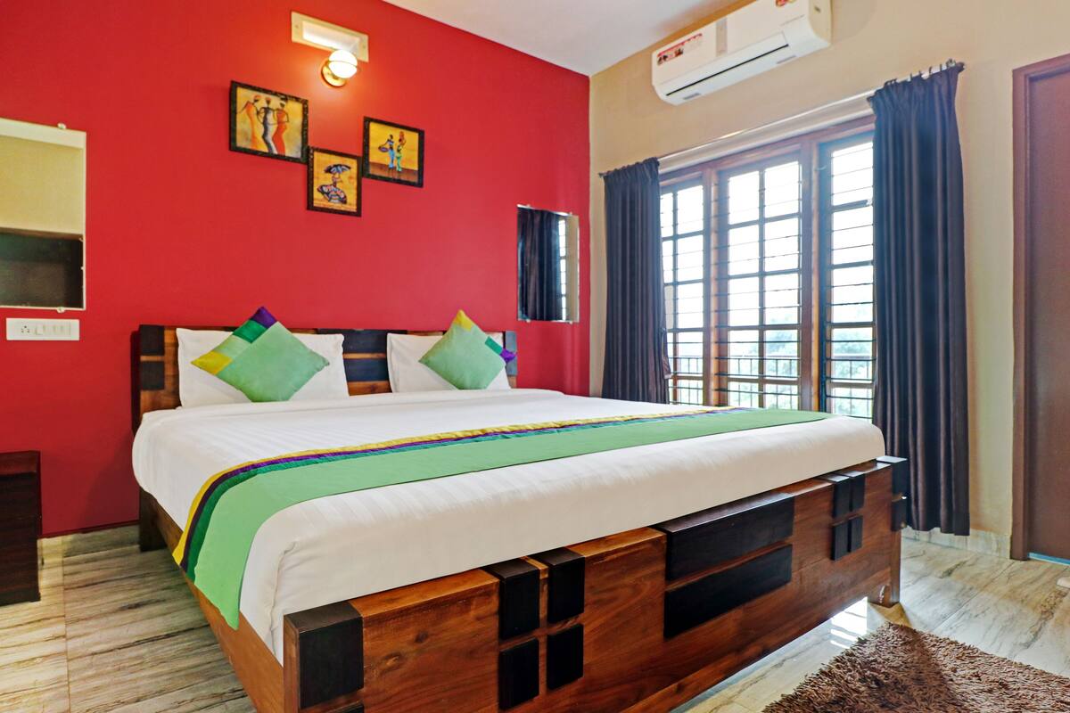 A bedroom with a wooden bed frame, a red wall, and a window with curtains.