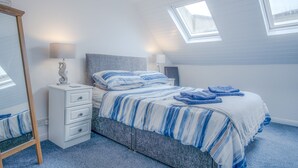 Une chambre à coucher comprenant un lit, une table de chevet, une commode et un miroir. Le plafond est doté de fenêtres de toit.