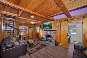 Un intérieur en bois avec une cheminée, un canapé en cuir et un téléviseur fixé au mur.