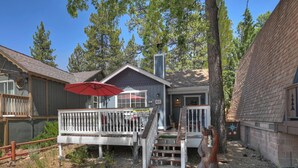 A wooden deck with a red umbrella, a staircase leading to a house, and a bear statue.