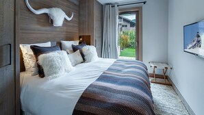 A modern bedroom with a large bed, wooden paneling, a mounted skull decoration, and a television on the wall. - Charming Garden-Level Apartment in Rochebrune, Megève – Sleeps 6 (Megève)