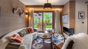 A cozy living room with a sofa, a TV, and a view of a balcony with outdoor furniture. - Charming Garden-Level Apartment in Rochebrune, Megève – Sleeps 6 (Megève)