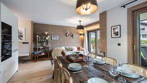 A modern kitchen with wooden flooring, a dining table set for four, and a large window offering a view of the outdoors. - Charming Garden-Level Apartment in Rochebrune, Megève – Sleeps 6 (Megève)
