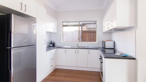 A modern kitchen with white cabinets, a stainless steel refrigerator, a microwave, and a sink. - 9 Breckenridge Street (Forster)