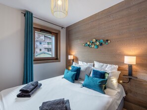 Relax in a spacious room with a large bed, featuring white bedding and multiple pillows, and enjoy a view of the city from the window.