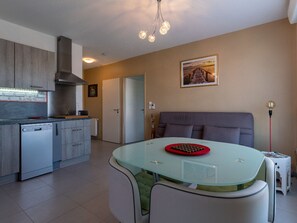 A modern kitchen with a glass dining table, a grey sofa, and a painting on the wall.