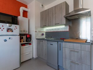 A modern kitchen with grey cabinets, a white refrigerator, a built-in oven, and a stainless steel range hood.