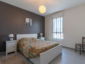 A bedroom with a bed, bedside tables, a chair, a window, and a wall-mounted picture.