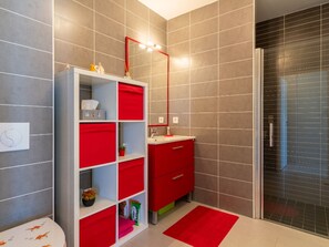 A bathroom with grey tiled walls, a white and red cabinet, a mirror, and a shower area. - Apartment in city center - 4 guests (Biscarrosse)