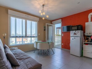 A compact living space with a kitchenette, a dining area with a table and chairs, a sofa, and a large window.