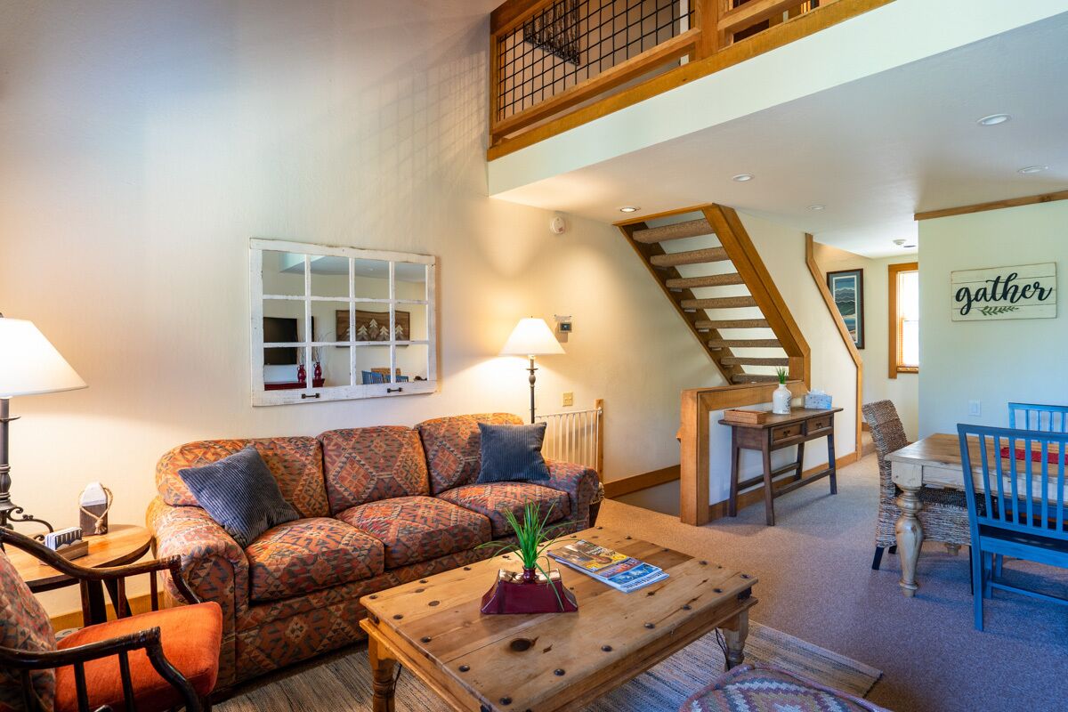 A spacious living room with a high ceiling, a wooden staircase, a dining area, and a cozy sofa set.