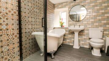 Un baño con pared de azulejos estampados, una bañera independiente, un lavamanos sobre pedestal y un inodoro.
