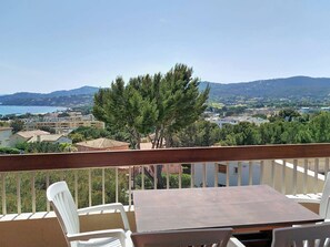 Un balcón con mesa y sillas, con vistas a un pueblo costero con edificios y colinas.