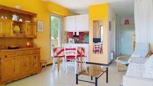 A bright yellow room with wooden cabinets, a dining table with chairs, a sofa, and a glass table. - Quiet studio with terrace in Bormes-les-Mimosas (Bormes-les-Mimosas)