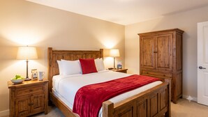 Een slaapkamer met een houten bed, twee nachtkastjes met lampen, een rode plaid en een houten garderobe.