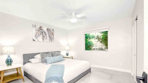 Une chambre à coucher avec un lit, un ventilateur de plafond, une fenêtre donnant sur un beau paysage et une table de chevet avec une lampe.