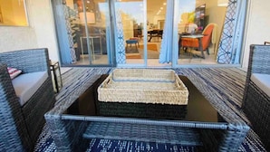 Un patio ensoleillé, agrémenté de meubles en osier et d’un tapis tissé, qui donne accès par une porte-fenêtre coulissante à un espace de salle à manger intérieur.